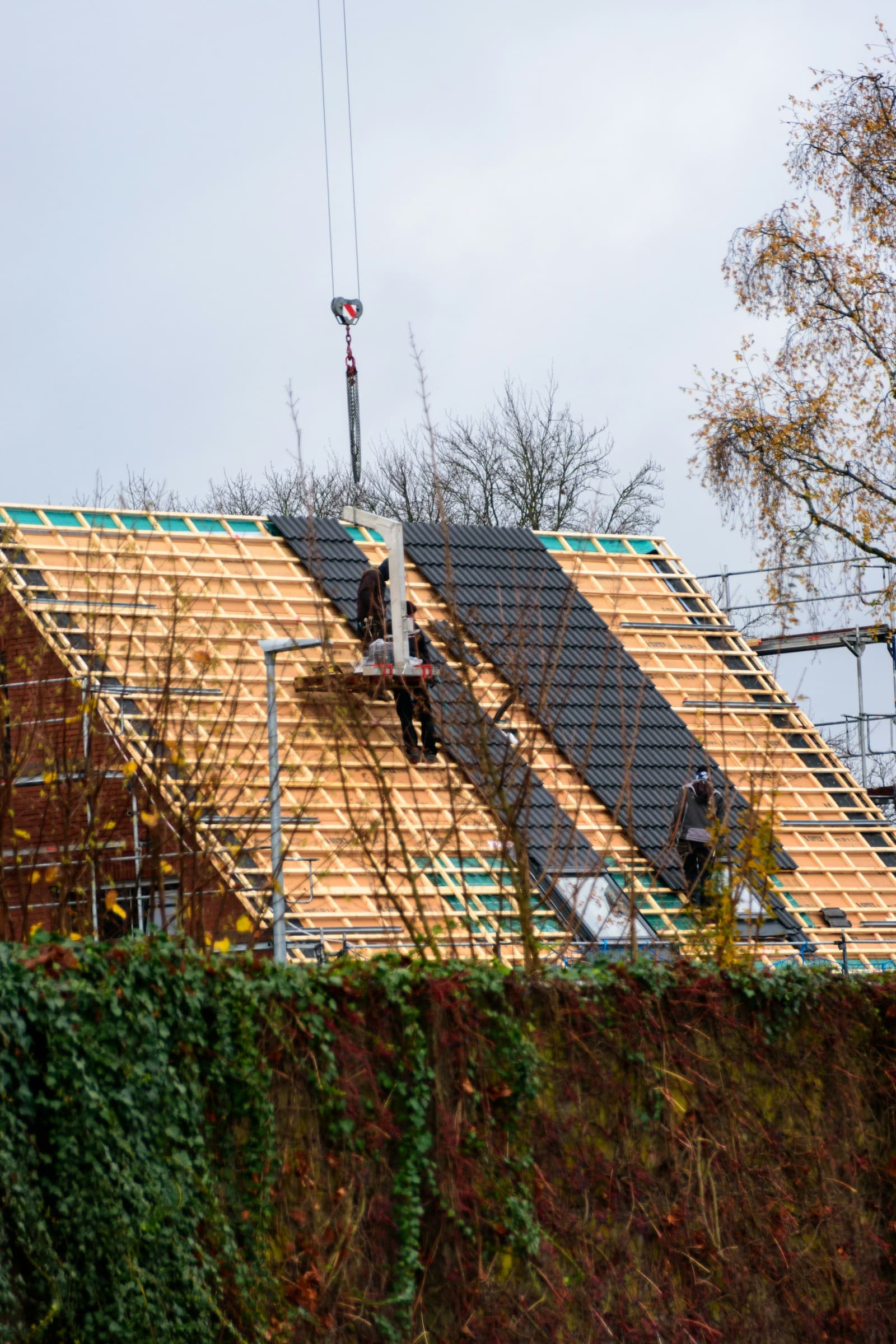 Charpente en bois recouverte de tuiles sombres en cours de pose